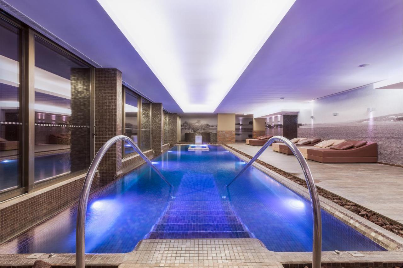Ap Lago Montargil - Conference & Spa Exterior photo The photo shows a modern indoor swimming pool area. The pool features a sleek design with steps leading into the water and a gentle curve at the sides. The water is illuminated in a blue hue, enhancing the relaxing atmosphere. Surrounding the pool ar
