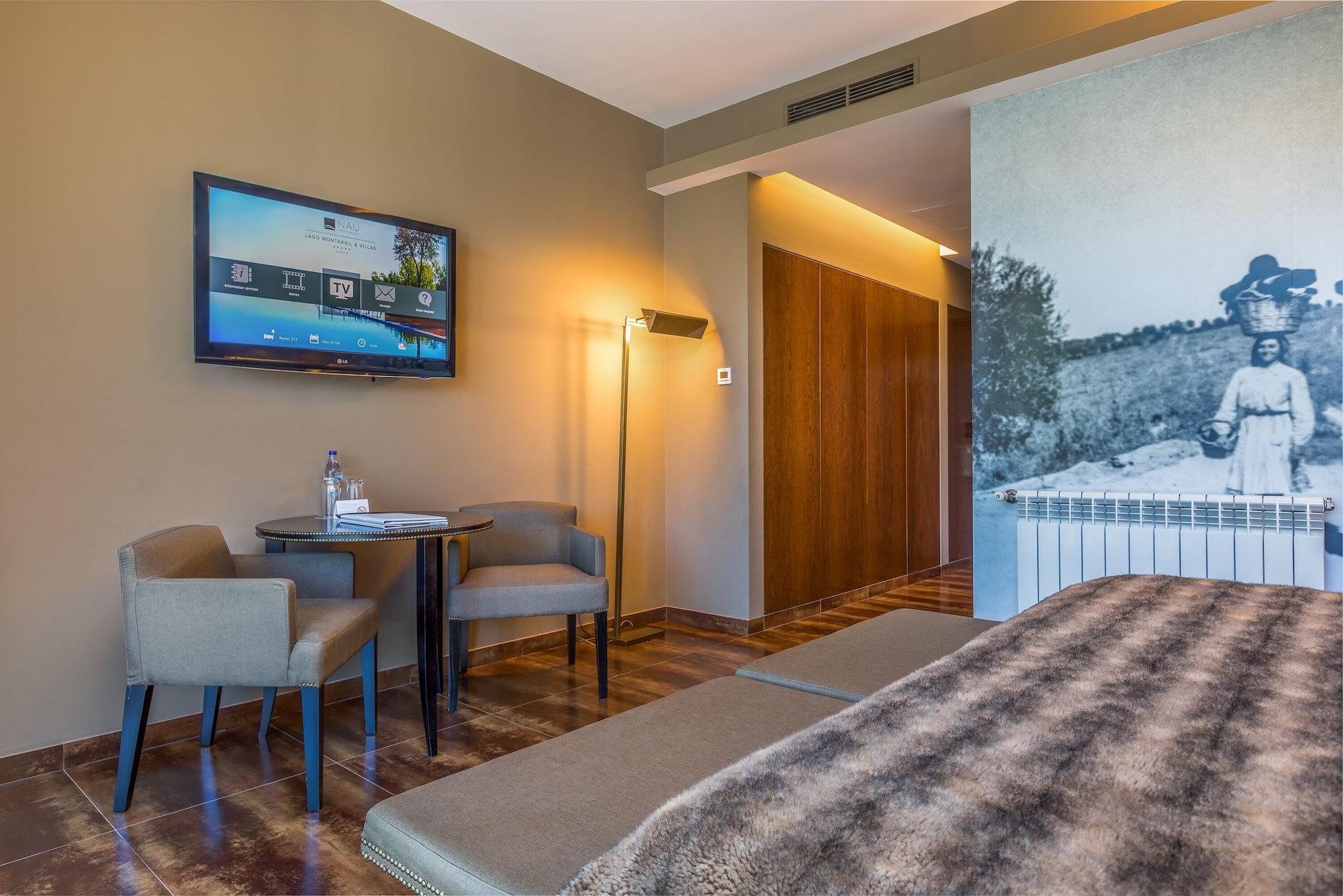 Ap Lago Montargil - Conference & Spa Exterior photo The photo shows an interior of a room, likely a hotel or a modern living space. In the foreground, there is a bed with a textured brown blanket. To one side, there are two comfortable chairs and a small table, possibly with a bottle of water. A flat-