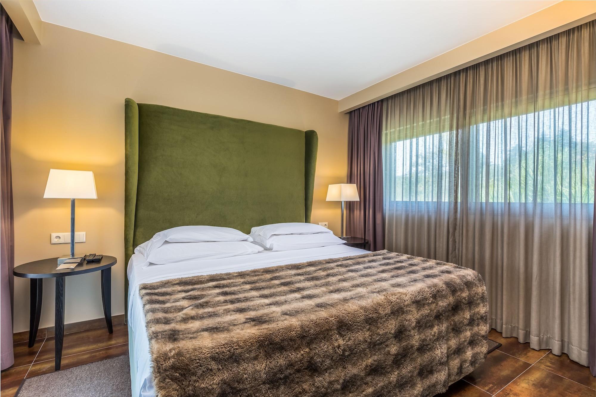 Ap Lago Montargil - Conference & Spa Exterior photo The photo shows a cozy hotel room featuring a large bed with two white pillows and a fur-style blanket draped over it. Behind the bed is a tall, green headboard that adds a touch of color to the room. On either side of the bed are bedside tables, eac