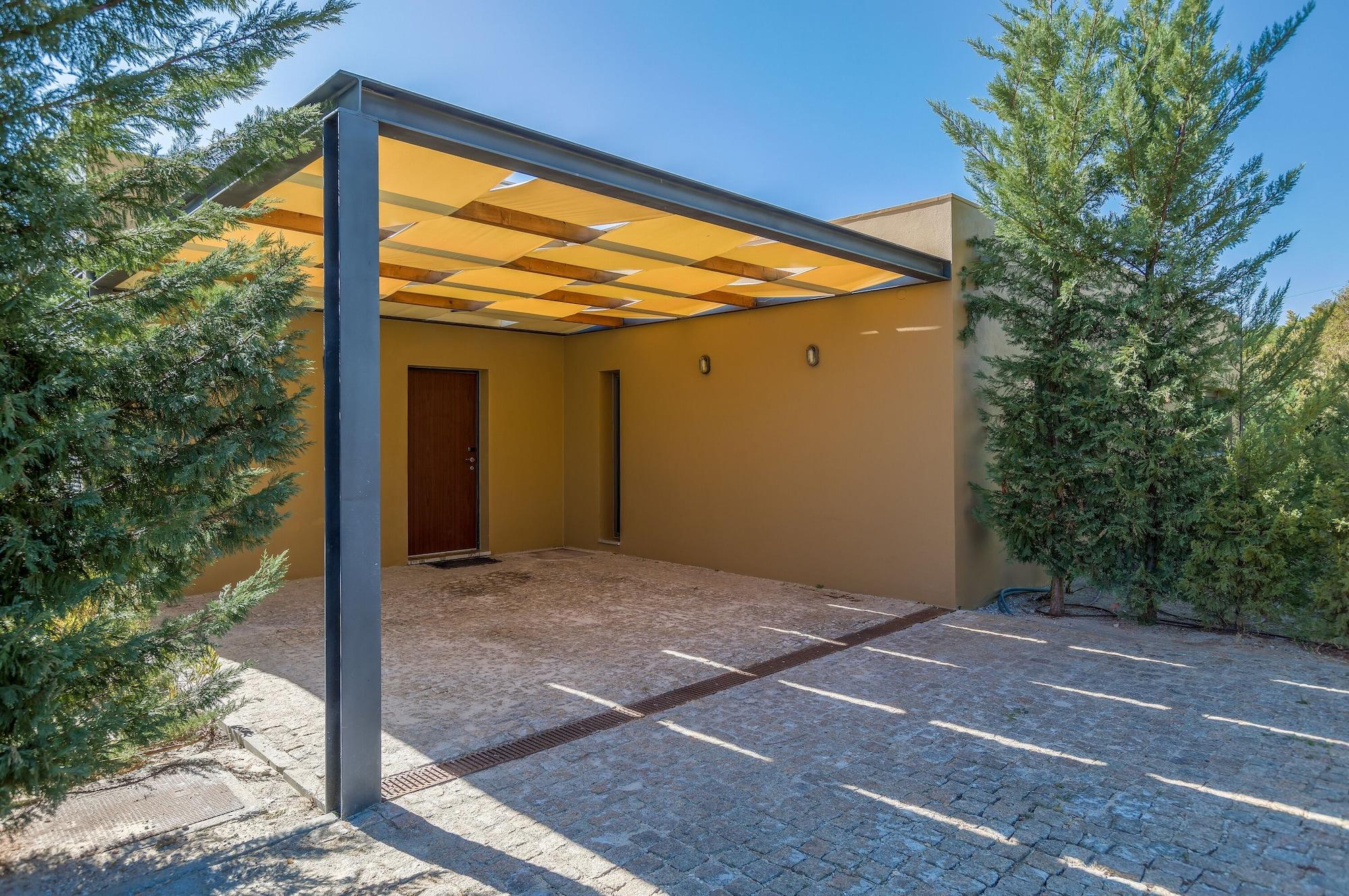 Ap Lago Montargil - Conference & Spa Exterior photo The photo shows an exterior view of a modern structure with a carport. The carport has a sleek, metallic frame and a yellowish canopy above it. In front of the structure, there is a paved area made of stone or tiles. The main entrance features a wood