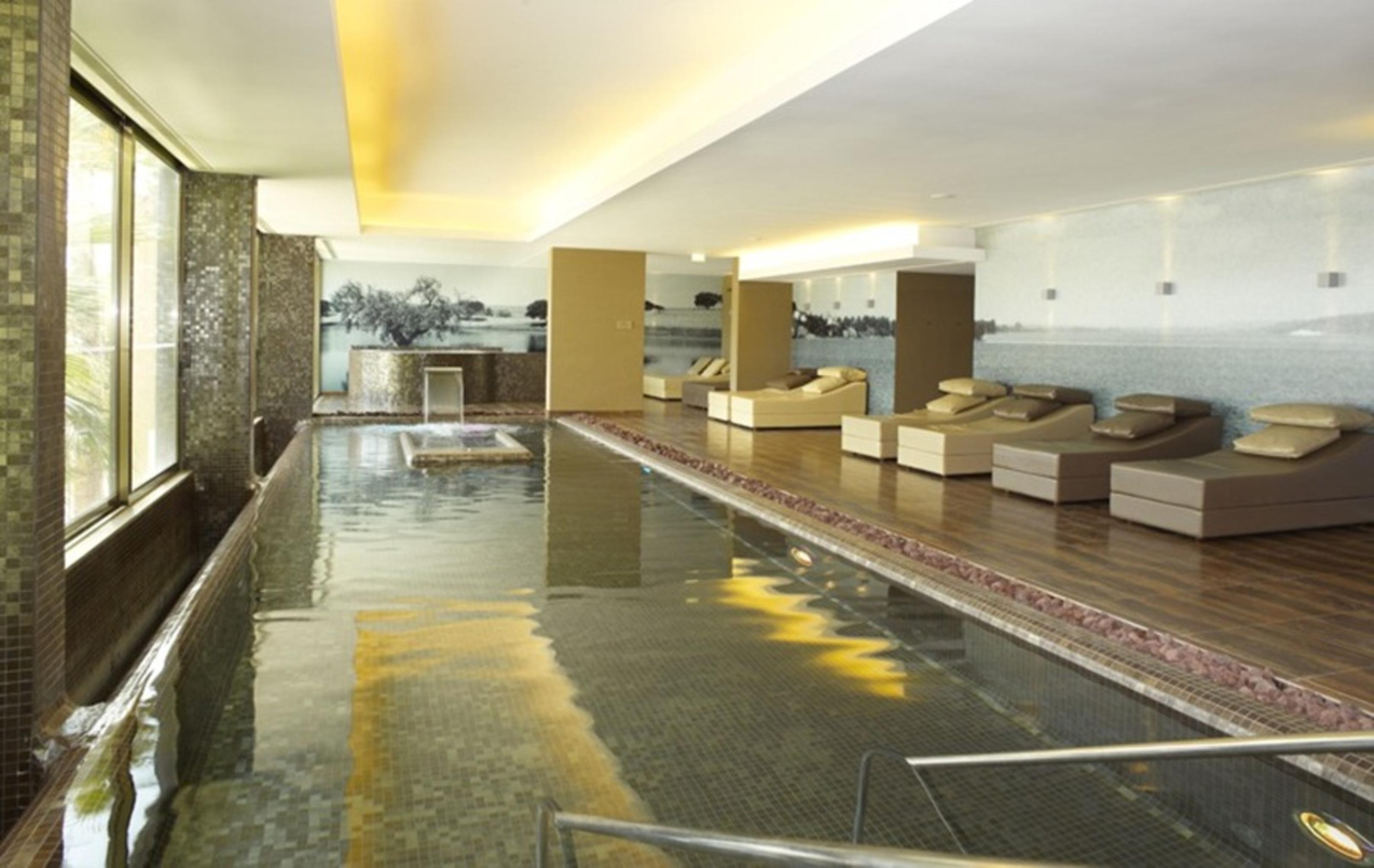 Ap Lago Montargil - Conference & Spa Exterior photo The photo shows a modern, serene spa environment. There is a swimming pool with calm water, reflecting the surrounding decor. Along the sides, there are several comfortable lounge chairs arranged, perfect for relaxation. Large windows allow natural l