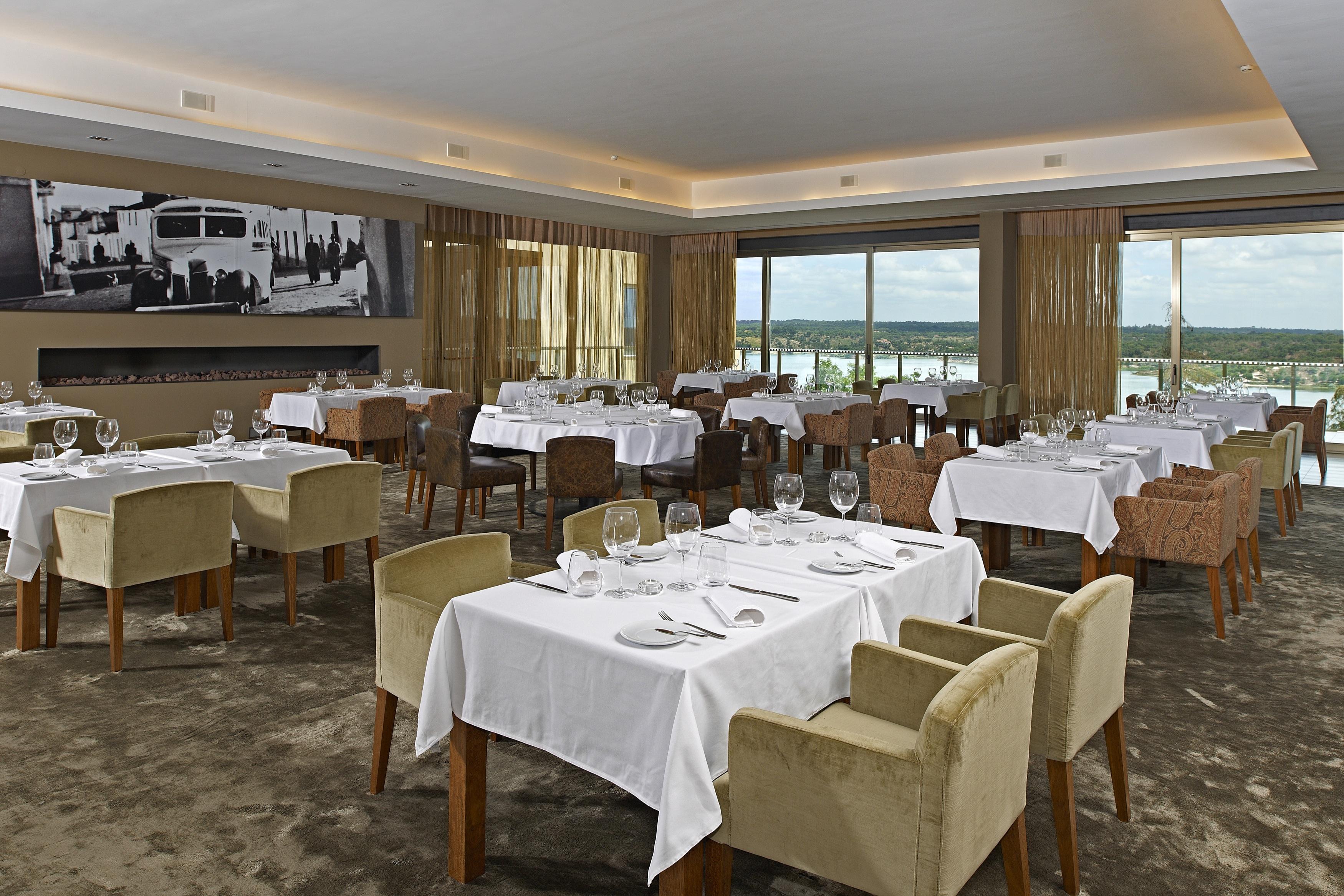 Ap Lago Montargil - Conference & Spa Exterior photo The photo shows an elegant restaurant interior featuring neatly arranged tables with white tablecloths. Each table is set with plates, cutlery, and glasses. The seating includes a mix of upholstered chairs in different colors—some light and others da