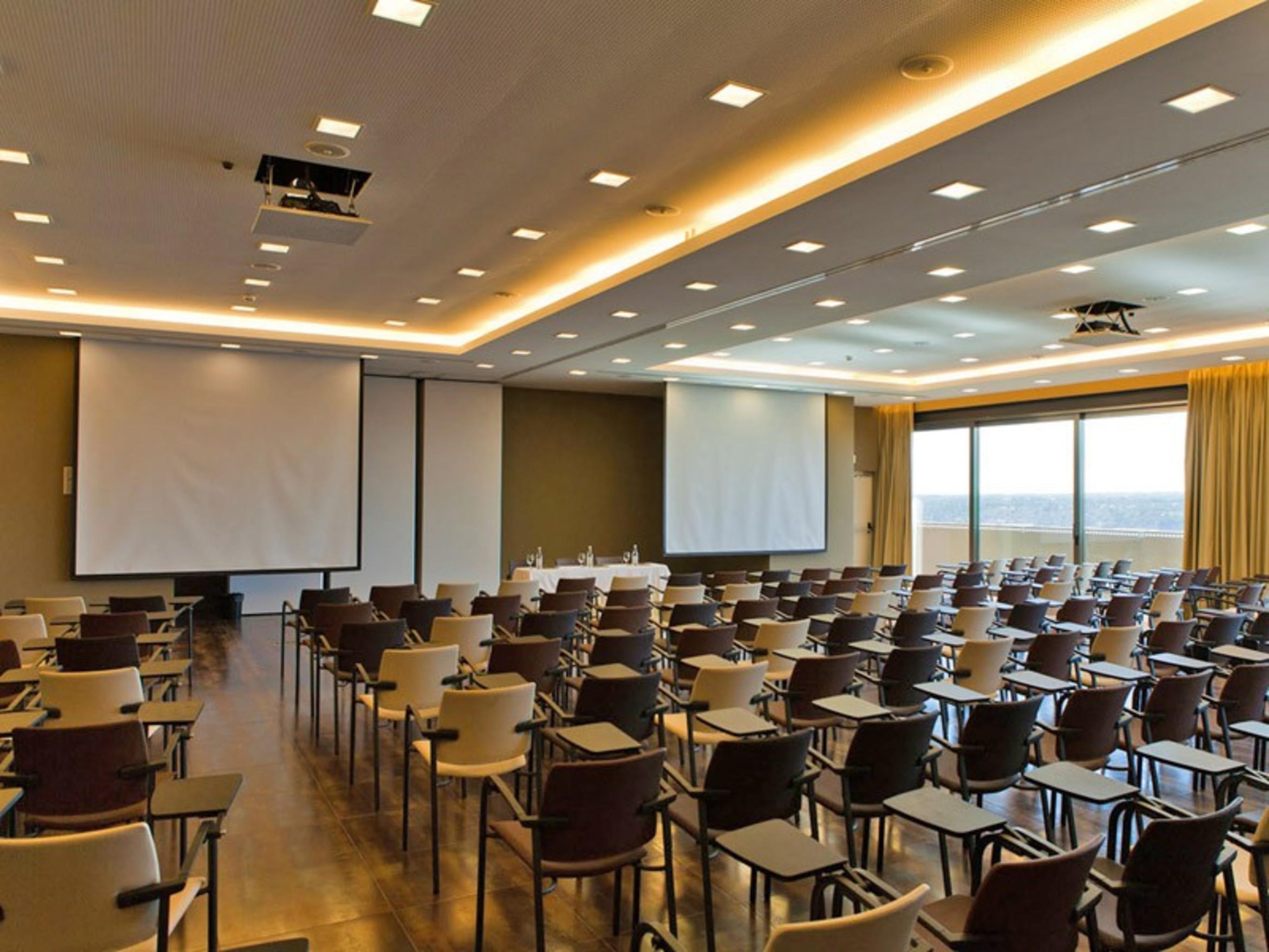 Ap Lago Montargil - Conference & Spa Exterior photo The photo shows a large conference room set up for a presentation or meeting. There are multiple rows of chairs arranged in a semi-theater style, facing two large projection screens. The room has a modern design, with soft lighting and large windows 