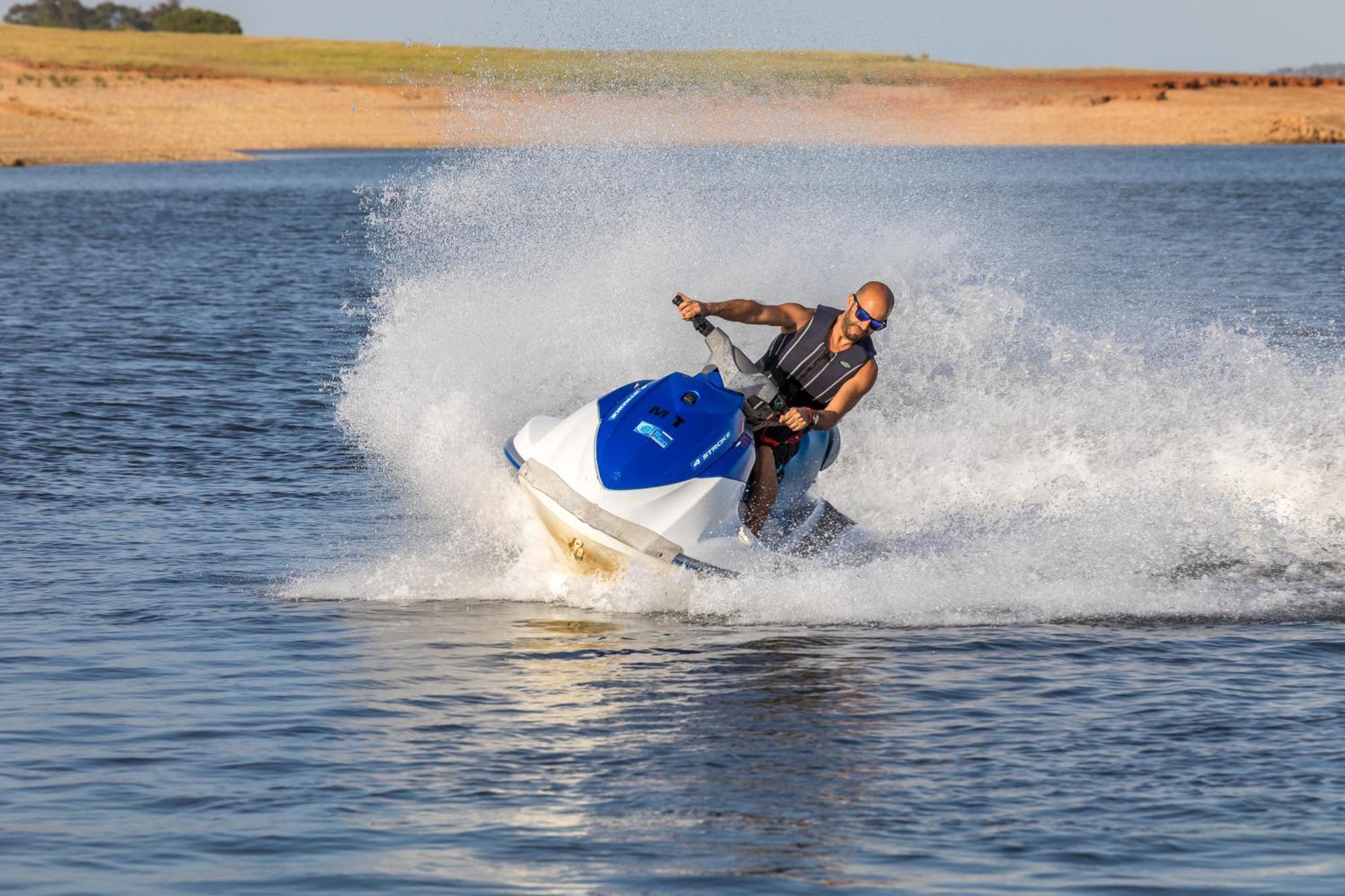 Ap Lago Montargil - Conference & Spa Exterior photo The photo shows a person riding a jet ski over a body of water. The rider is wearing sunglasses and a life vest, leaning forward as the jet ski accelerates, creating a spray of water around them. The background features a natural landscape, likely a 